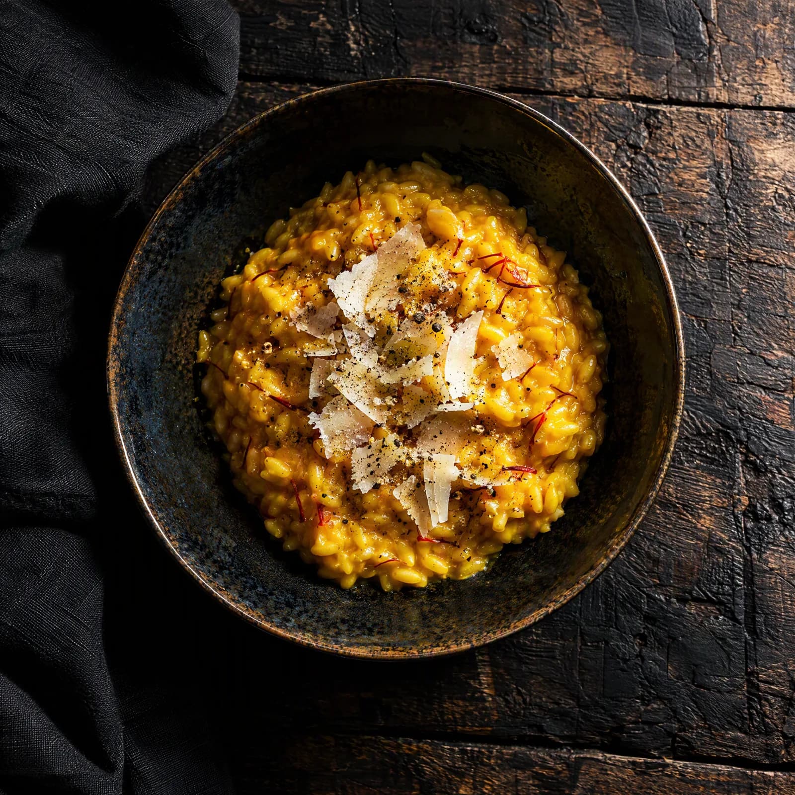 Overhead frame of saffron risotto in a dark-glazed bowl on a charred wooden table