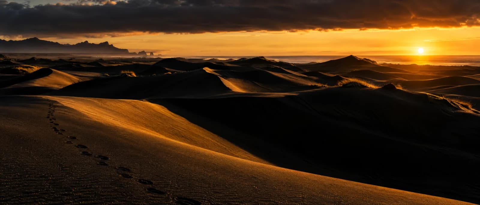 Ultra-wide 21:9 panorama of black volcanic sand dunes under a low amber sun